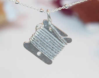 Puede incluir: Un collar de plata con un dije con forma de carrete de hilo.
