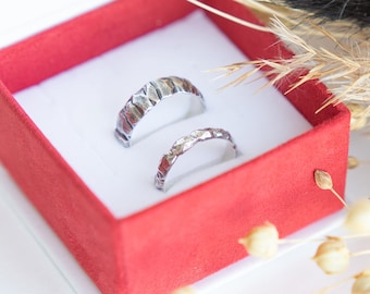 May include: Two silver wedding bands with a textured finish, displayed in a red velvet ring box.