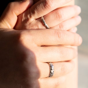 May include: Two silver rings on a person's fingers. Both rings are textured and have a hammered finish.