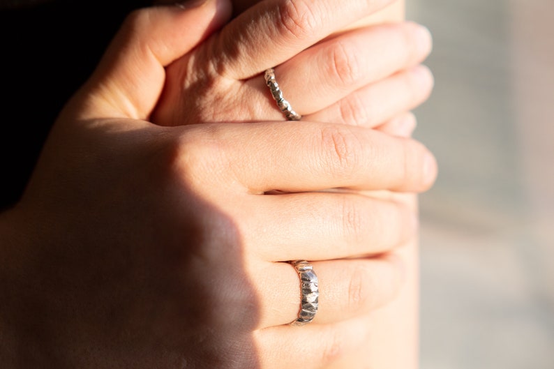 May include: Two silver rings on a person's fingers. Both rings are textured and have a hammered finish.