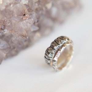 May include: A silver ring with a textured, hammered finish. The ring has a thin band of gold running along the top.