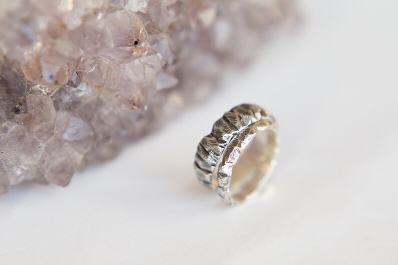 May include: A silver ring with a textured, hammered finish. The ring has a thin band of gold running along the top.