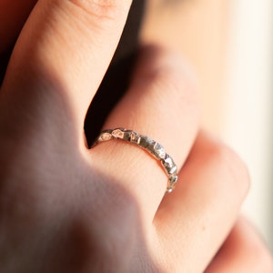 May include: A silver ring with a textured, hammered finish. The ring is worn on a finger.