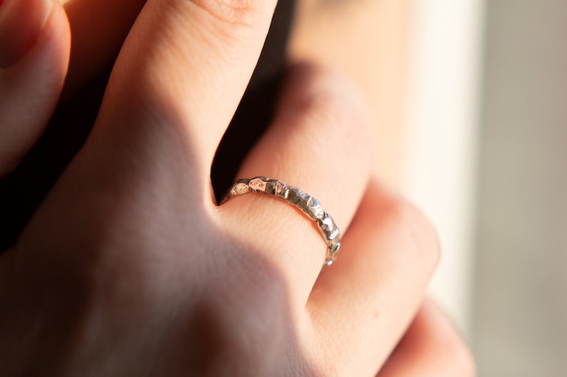 May include: A silver ring with a textured, hammered finish. The ring is worn on a finger.