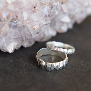 May include: Two silver rings with a textured, hammered finish. The rings are stacked on top of each other and are resting on a dark grey surface.