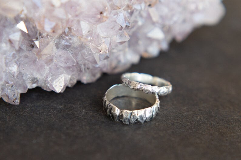May include: Two silver rings with a textured, hammered finish. The rings are stacked on top of each other and are resting on a dark grey surface.
