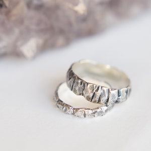 May include: Two silver rings with a textured, hammered finish. The rings are stacked on top of each other.