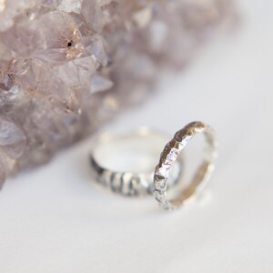 May include: Two silver rings with a textured, hammered finish. The rings are stacked on top of each other and are resting on a white surface.