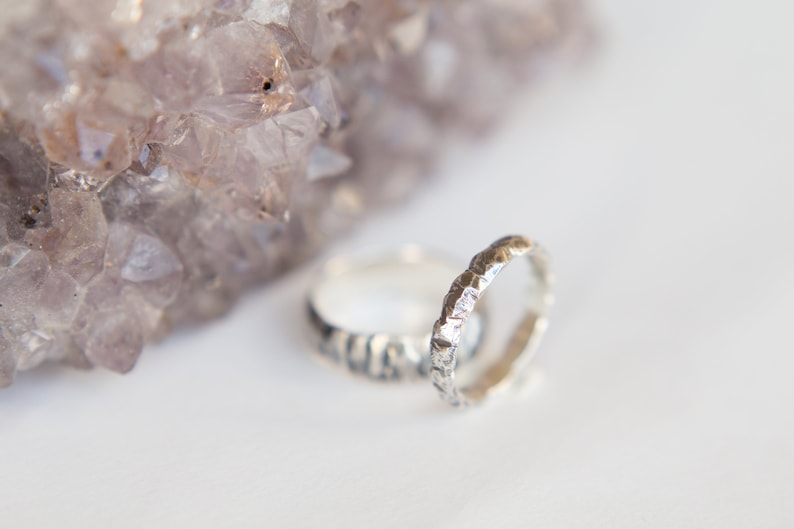 May include: Two silver rings with a textured, hammered finish. The rings are stacked on top of each other and are resting on a white surface.