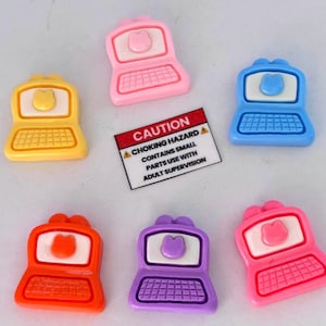May include: Six small plastic laptop-shaped charms in yellow, pink, blue, orange, purple, and bright pink, each featuring a white screen with a raised cat head icon and a grid keyboard. A rectangular white warning label reads CAUTION CHOKING HAZARD.