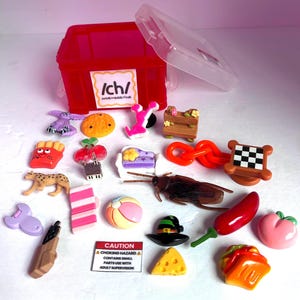 May include: A red plastic storage bin with a lid and a label reading /ch/ initial/medial/final, surrounded by various miniature plastic charms including a cheetah, a cockroach, a chili pepper, a peach, a slice of cheese, and a checkerboard table.