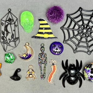 Może przedstawiać: Kolekcja zawieszek i ozdób o tematyce Halloween. Zawiera czarną pajęczynę, kapelusz czarownicy, fioletowe serce, zieloną czaszkę, czarnego pająka, fioletowy księżyc, szkielet i butelkę z korkiem.