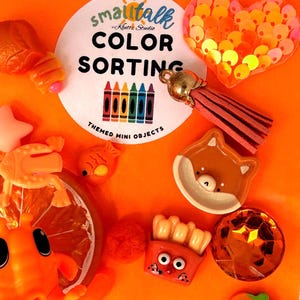 May include: A collection of orange-themed miniature objects including a circular label reading Smalltalk Klutz Studio Color Sorting Themed Mini Objects, a sequined heart, a tassel, a fox face, a french fry container, and a pumpkin figurine.