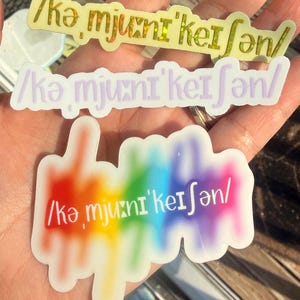 May include: Three stickers with the text "/kə, mju:ni' keı ∫ən/". The top sticker is yellow with holographic accents. The middle sticker is light purple. The bottom sticker has a rainbow gradient background.