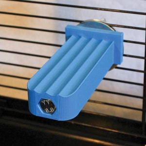Pode incluir: Um poleiro retangular azul-claro impresso em 3D com uma superfície superior ranhurada e uma cabeça de parafuso hexagonal embutida na face frontal. O poleiro é montado horizontalmente numa parede de gaiola de arame preta.
