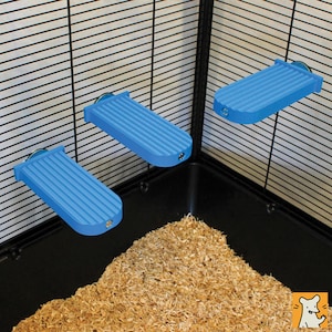 May include: Three rectangular blue platforms with a ribbed surface texture, each featuring a small metallic attachment point at the front edge. These platforms are mounted horizontally to the interior wire grid walls of an animal enclosure.