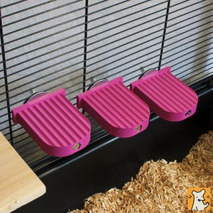 May include: Three bright pink, semi-circular platforms with a ribbed, textured surface. Each platform features a flat back edge with a metal bolt and nut mechanism for attachment to a black wire cage wall, providing a horizontal surface.