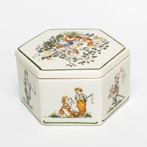 Op de afbeelding: Een witte keramische mok met een zwarte handgreep en de tekst "But First, Coffee" in een vetgedrukte, zwarte letter. De mok staat tegen een vage achtergrond, wat een gezellige setting suggereert.