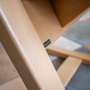 May include: Close-up of a wooden chair frame with a light finish. The frame is constructed with angled supports and a seat. A small black label with the word "VARIER" is visible.