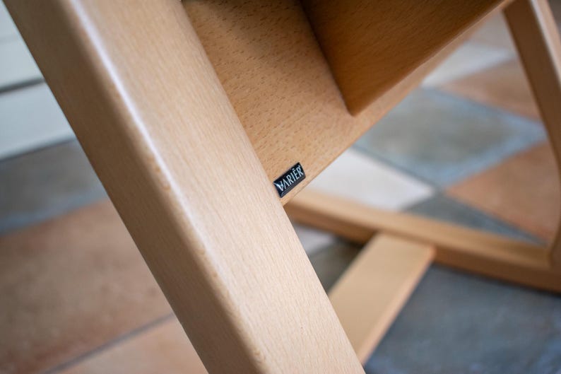 May include: Close-up of a wooden chair frame with a light finish. The frame is constructed with angled supports and a seat. A small black label with the word "VARIER" is visible.