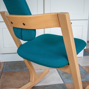 May include: A teal-colored seat and backrest chair with a light wood frame. The chair has a curved design with a padded seat and back support. The chair is designed for comfort and support.