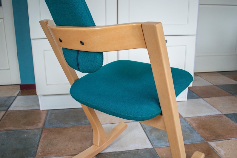 May include: A teal-colored seat and backrest chair with a light wood frame. The chair has a curved design with a padded seat and back support. The chair is designed for comfort and support.