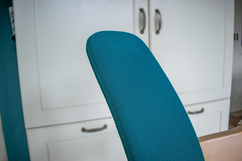 May include: Close-up of a teal-colored chair back with a textured fabric. The chair back is curved and set against a white cabinet with dark handles. The chair is part of a furniture set.