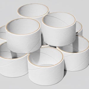 Puede incluir: Una pila de tubos de cartón blancos, dispuestos en forma de pirámide. Los tubos tienen un interior marrón claro y están hechos de un material de papel texturizado. Los tubos cilíndricos están vacíos, con una costura diagonal visible en el lateral.