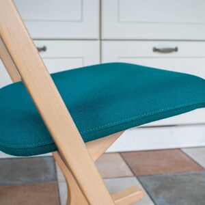 May include: A teal ergonomic kneeling chair with a wooden frame. The seat and knee rest are upholstered in a textured teal fabric. The chair's design promotes good posture and is suitable for home or office use.