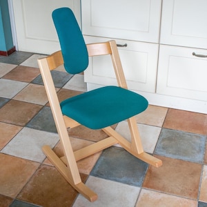 May include: A teal kneeling chair with a wooden frame. The chair has a padded seat and backrest, and a rocking base. The chair is designed to promote good posture and is suitable for use at a desk or table.