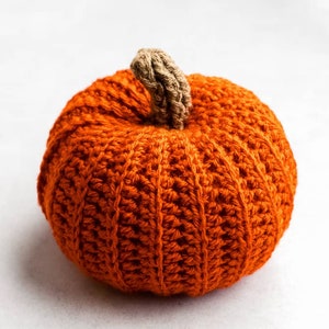 May include: A crocheted orange pumpkin with a brown stem. The pumpkin is made with a textured stitch and has a round shape.