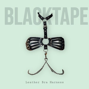 Könnte beinhalten: Schwarzer Leder-BH-Gurt mit silberner Hardware und einem Kettendetail. Der Gurt hat einen Choker-Ausschnitt und einen großen O-Ring in der Mitte. Der Text "BLACKTAPE" wird über dem Gurt angezeigt.