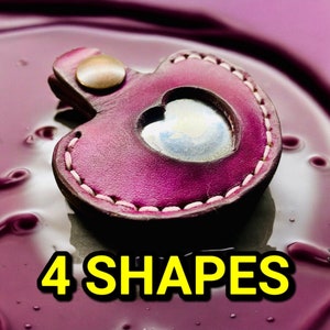 May include: A small, heart-shaped leather keychain with a pink hue and a stitched border. The keychain has a small, round, metal loop at the top and a heart-shaped cutout in the center. The text "4 SHAPES" is printed in yellow below the keychain.