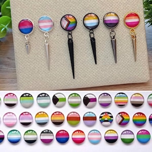 Könnte beinhalten: Ein Set mit 20 bunten runden Ohrringen mit verschiedenen Designs von Pride-Flaggen. Die Ohrringe sind aus Metall und haben einen baumelnden Dorn. Die Flaggen umfassen die bisexuelle, transgender, genderqueer, lesbische, pansexuelle und asexuelle Flagge.