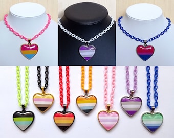May include: A set of ten necklaces with heart-shaped pendants featuring different pride flags. The necklaces are available in a variety of colors, including pink, white, blue, black, green, yellow, orange, and purple.
