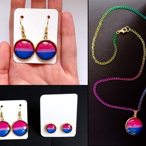 Peut inclure: Ensemble de bijoux avec des boucles d'oreilles et un collier arborant le drapeau de la fierté bisexuelle. Les boucles d'oreilles sont dorées avec un pendentif rond. Le collier a une chaîne arc-en-ciel. Des clous d'oreilles sont également présents.