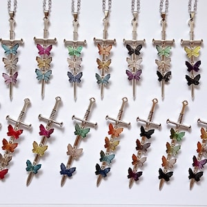 Puede incluir: Un conjunto de 10 collares de espada plateada, cada uno con tres dijes de mariposa. Las mariposas son de varios colores, incluyendo rojo, azul, verde, amarillo y morado.