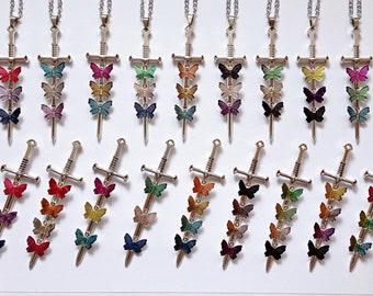 May include: A collection of silver-toned sword pendants, each featuring three small butterflies in various colors attached to the blade. The swords have detailed hilts and crossguards, and each pendant is suspended from a silver-toned chain.