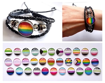 May include: A set of 20 different pride flag charm bracelets. Each bracelet features a different pride flag, including the rainbow, transgender, bisexual, and asexual flags. The bracelets are made of black leather and have silver beads.