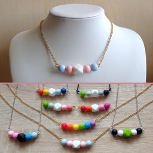 May include: A set of colorful silicone bead necklaces with different shapes and colors. The necklaces are on a gold chain and are displayed on a wooden surface.