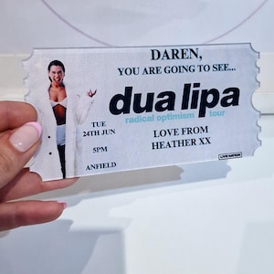 Pu&ograve; includere: Un biglietto bianco con una foto di Dua Lipa, il testo "DAREN, YOU ARE GOING TO SEE... dua lipa", "TUE 24TH JUN SPM ANFIELD", "radical optimism", e "LOVE FROM HEATHER XX".
