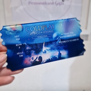 Pu&ograve; includere: Un biglietto blu e bianco per un concerto dei Coldplay. Il biglietto dice "Coldplay Music of the Spheres World Tour" e "Domenica 7 settembre 2023 Wembley Stadium". Il biglietto ha un numero di settore, fila e posto: Settore 550, Fila 5, Posto 330.