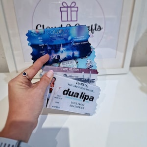 Pu&ograve; includere: Tre biglietti per concerti. Il biglietto in alto &egrave; per il tour Music of the Spheres dei Coldplay, il biglietto in mezzo &egrave; per Paul Heaton e il biglietto in basso &egrave; per Dua Lipa. Il biglietto di Dua Lipa dice "Daren, you are going to see... Dua Lipa" e "Love from Heather xx".