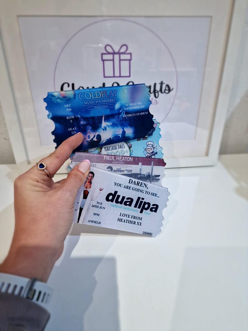 Pu&ograve; includere: Tre biglietti per concerti. Il biglietto in alto &egrave; per il tour Music of the Spheres dei Coldplay, il biglietto in mezzo &egrave; per Paul Heaton e il biglietto in basso &egrave; per Dua Lipa. Il biglietto di Dua Lipa dice "Daren, you are going to see... Dua Lipa" e "Love from Heather xx".