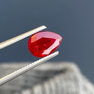 以下が含まれることがあります： 深い赤色の洋梨型のルビーの宝石。宝石はピンセットで保持されています。