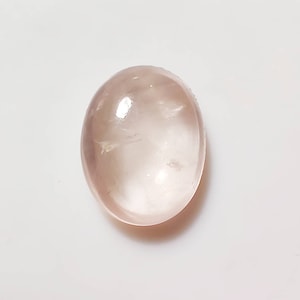 May include: A pale pink oval cabochon gemstone with a smooth, polished surface.