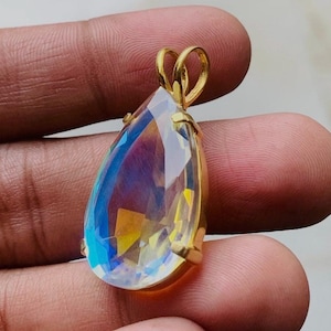 May include: A teardrop-shaped pendant with a gold-coloured setting. The large, faceted gemstone displays a spectrum of colours, including blue, yellow, and purple. The pendant has a loop at the top for a chain.