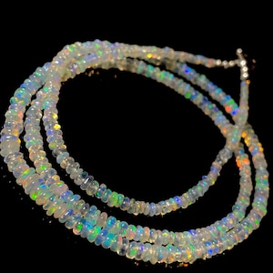 Puede incluir: Un collar de múltiples hilos hecho de cuentas de ópalo iridiscente. Las cuentas son pequeñas y redondas, y el collar es de color azul claro con destellos de verde, amarillo y naranja.