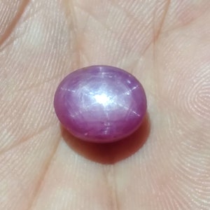 May include: A pink star ruby gemstone with a star-shaped reflection in the centre.