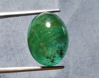 Pode incluir: Uma gema verde oval cabochão com uma superfície lisa e polida. A pedra é translúcida e tem inclusões visíveis.